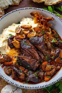 a bowl filled with meat, potatoes and carrots on top of a wooden table