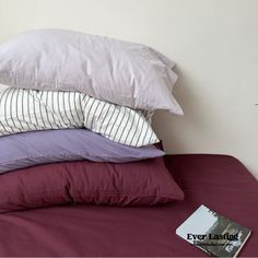 a stack of pillows sitting on top of a bed next to a book and plant