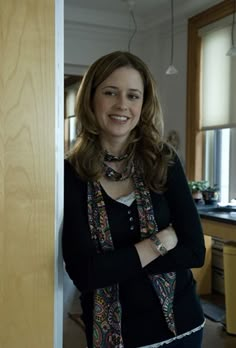 a woman standing in front of a door with her arms crossed and wearing a scarf around her neck