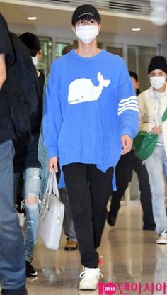 a man in a blue sweater and mask walks through an airport with other people behind him