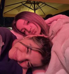 two women are laying down together under an umbrella in the rain and smiling at the camera