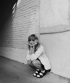 a woman kneeling down next to a brick wall