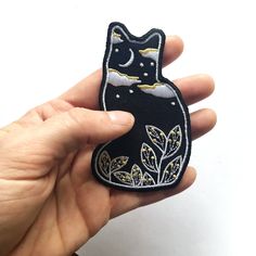 a hand holding a black and white cat patch with leaves on it's side