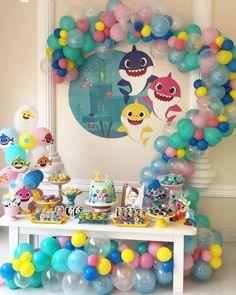 a birthday party with balloons, cake and other items on the table in front of a shark balloon arch