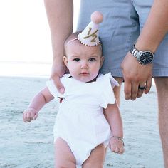 a baby is wearing a birthday hat while being held by its parent on the beach