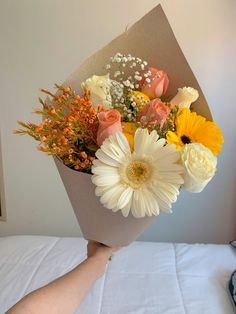 a person holding a bouquet of flowers on top of a white tablecloth covered bed