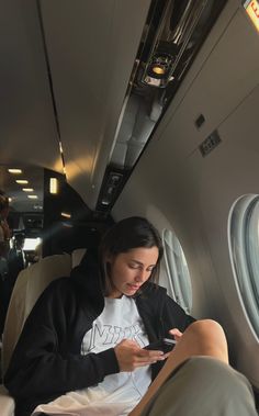 a woman sitting on an airplane looking at her cell phone