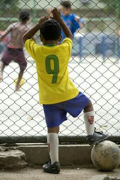 a young boy playing soccer in front of a chain link fence with other children behind him