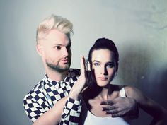 a man standing next to a woman in front of a white wall with checkered shirt on