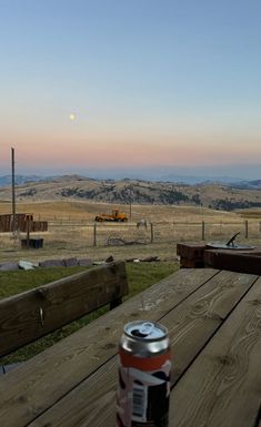 a can of beer sitting on top of a wooden table next to a fence and field