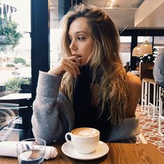 a woman sitting at a table with a cup of coffee in front of her face