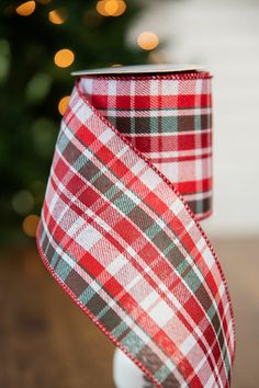 a red and green plaid ribbon on a white cup with a christmas tree in the background