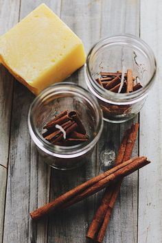 some cinnamon sticks and cheese are on a wooden table next to two small glass jars