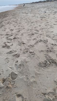 two people walking on the beach with footprints in the sand