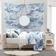 a bed with blue and white clouds on the wall next to a mirror hanging above it