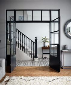 a living room with a white couch and black framed glass doors leading to the second floor