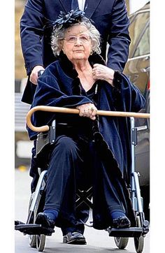 an older woman in a wheelchair being pushed by a man with a cane and suit on