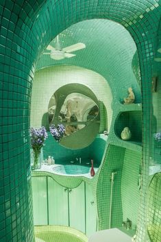 a bathroom with green tiled walls and a round mirror above the sink in front of it