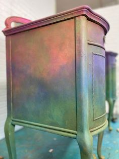 an old metal cabinet painted purple and green with pink accents on the top, sitting on a blue surface