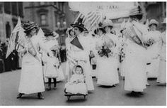 an old black and white photo shows women in dresses with flags on their heads walking down the street