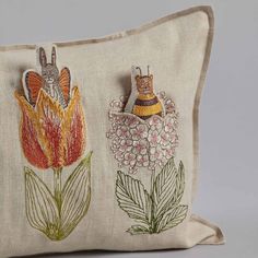 an embroidered pillow with two bugs and flowers on the front, sitting on a gray surface