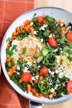 a pan filled with vegetables and cheese on top of a wooden table next to an orange napkin