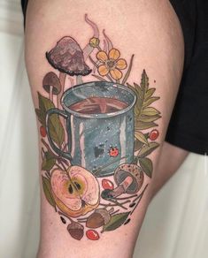 a cup of coffee on the thigh with flowers and leaves around it, surrounded by mushrooms