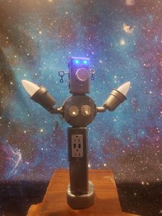 a toy robot with its arms outstretched on a wooden platform in front of a space background