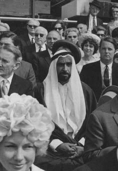 a group of people sitting next to each other in front of a building and one person wearing a headscarf