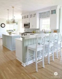 a large kitchen with white cabinets and wooden flooring, along with bar stools