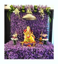 an idol sitting on top of a purple flower covered table next to a bell and potted plant