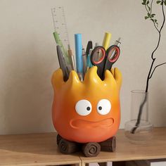 an orange container with scissors, pens and pencils in it sitting on a table