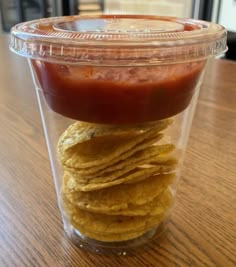 a plastic container filled with tortilla chips and ketchup on top of a wooden table