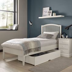 a white bed with drawers underneath it in a room that has blue walls and hardwood floors