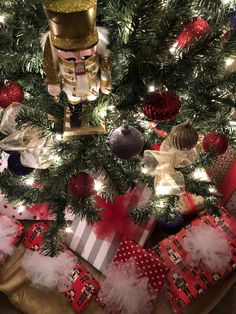 a christmas tree with presents under it and a nutcracker figurine on top