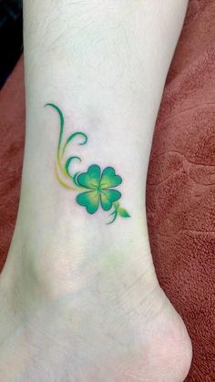 a green clover tattoo on the foot of a woman's leg, which is decorated with four leaf clovers