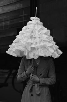 black and white photograph of woman in trench coat holding an umbrella over her head with ruffles on it