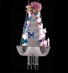 a three tiered cake with butterflies and flowers on the top is suspended from a chandelier