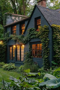 a black house with ivy growing on the side and windows that are lit up at night