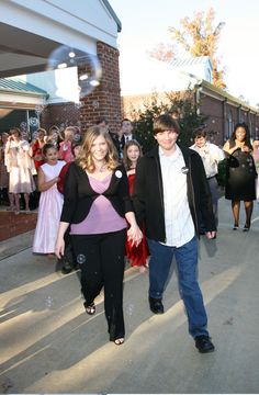 a man and woman are walking down the street with people in the background holding hands