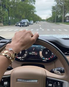 a hand on the steering wheel of a car driving down a road with trees in the background