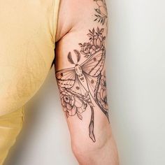 a woman with a tattoo on her arm holding onto a yellow t - shirt that has flowers and a butterfly on it