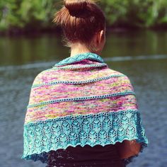 a woman wearing a knitted shawl looking out over the water from her back