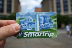 a hand holding up a small business card in front of some buildings and people walking on the street