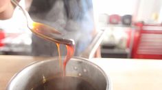 a person pouring sauce into a pot on top of a wooden table with a spoon