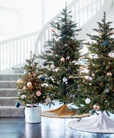 two christmas trees are sitting on the floor in front of a banister and stairs