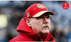 an older man wearing a red jacket and hat on the sidelines at a football game