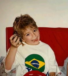 two children sitting on a red couch and one is holding a cell phone to his ear