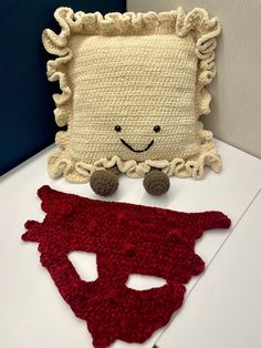 a crocheted pillow with a red cape on it next to a knit mask