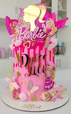 a pink birthday cake with barbie dolls on it's top and the words barbie dream written in gold